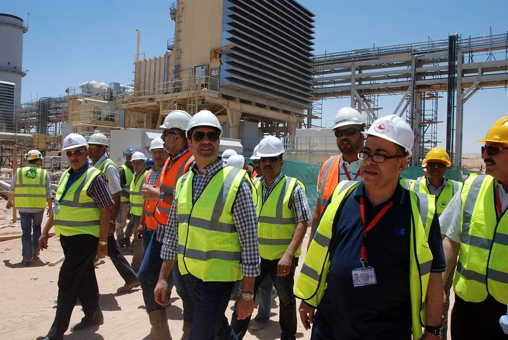 Site personnel in high-visibility vests walking in front of gas turbine generation units under construction