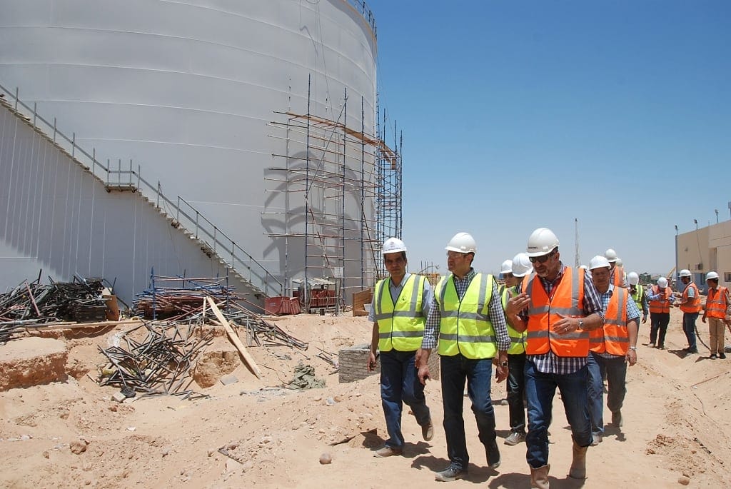 Site team walking past a large storage tank wrapped in scaffolding during erection