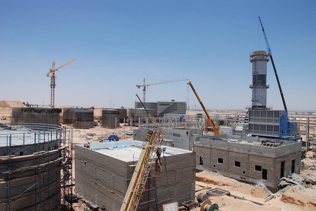 Power plant under construction, with storage tanks at various stages of erection, tower cranes and a stack