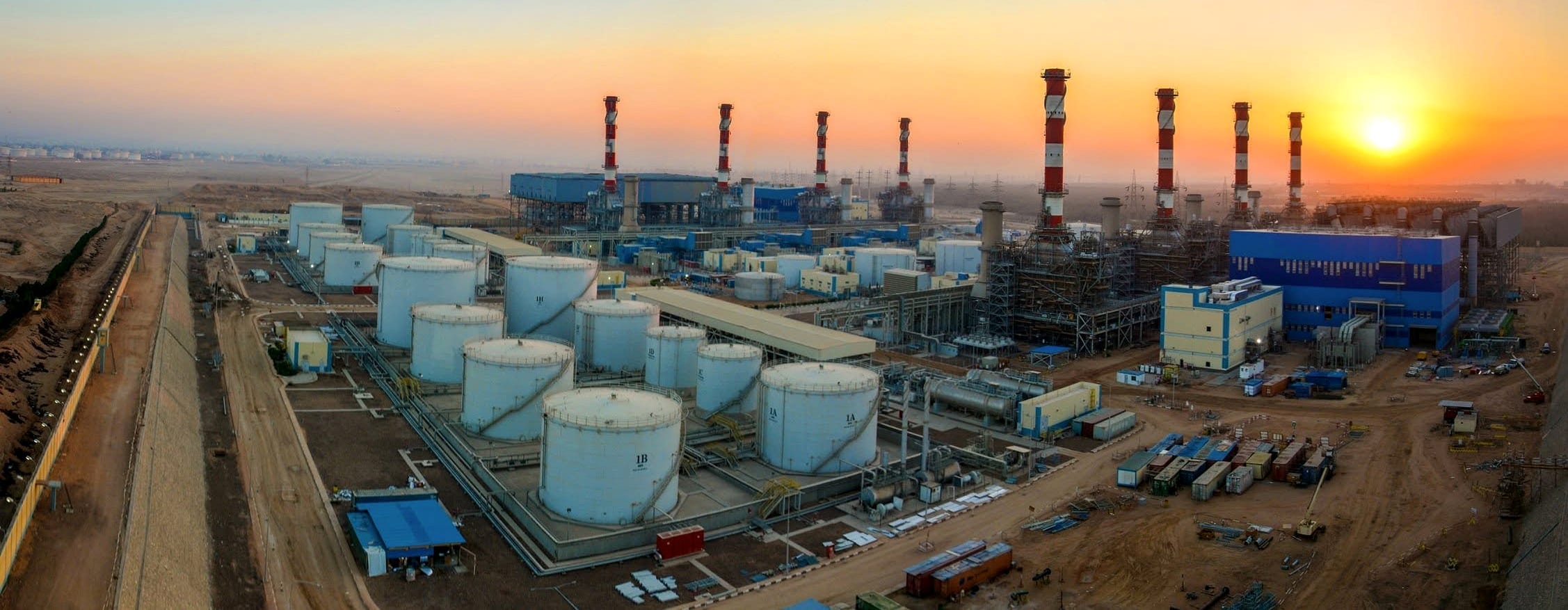 Aerial panorama of a power plant tank farm at sunset, with storage tanks, stacks and generation units