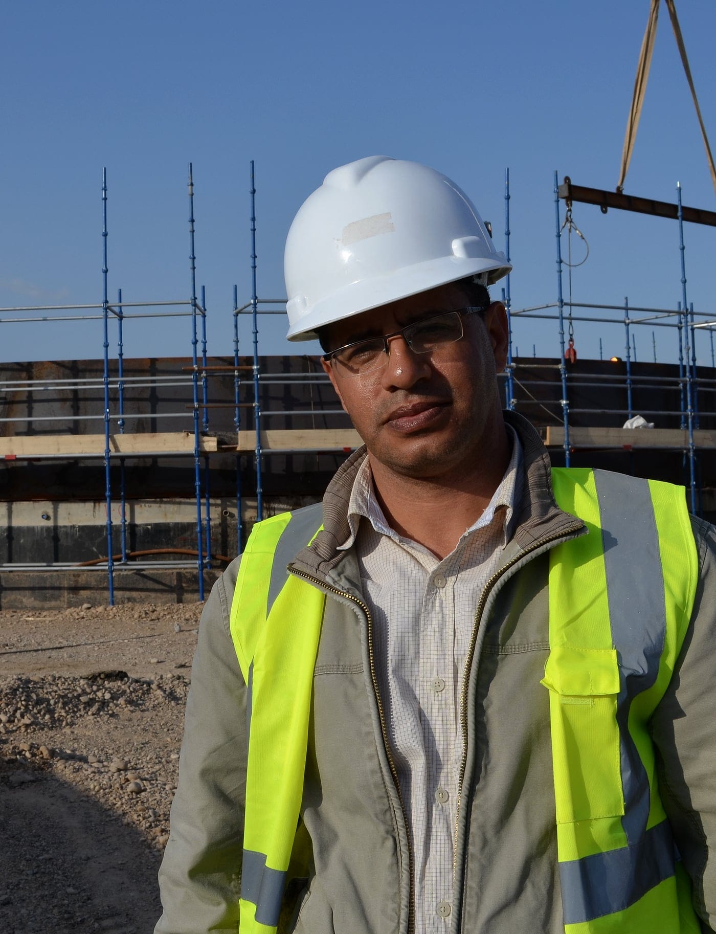TEMCO's founder on site in hard hat and high-visibility vest, with a storage tank under construction and a crane behind