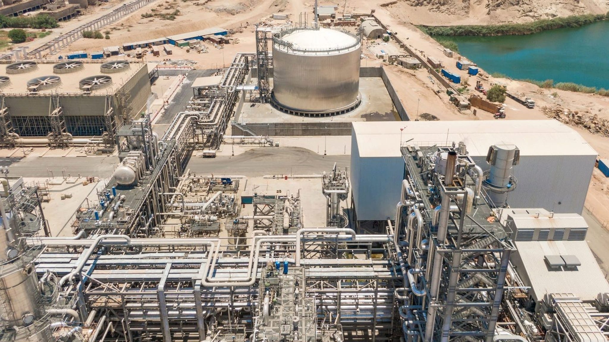 Aerial view of an industrial process plant beside the Nile, with piping racks, cooling towers and a large domed storage tank