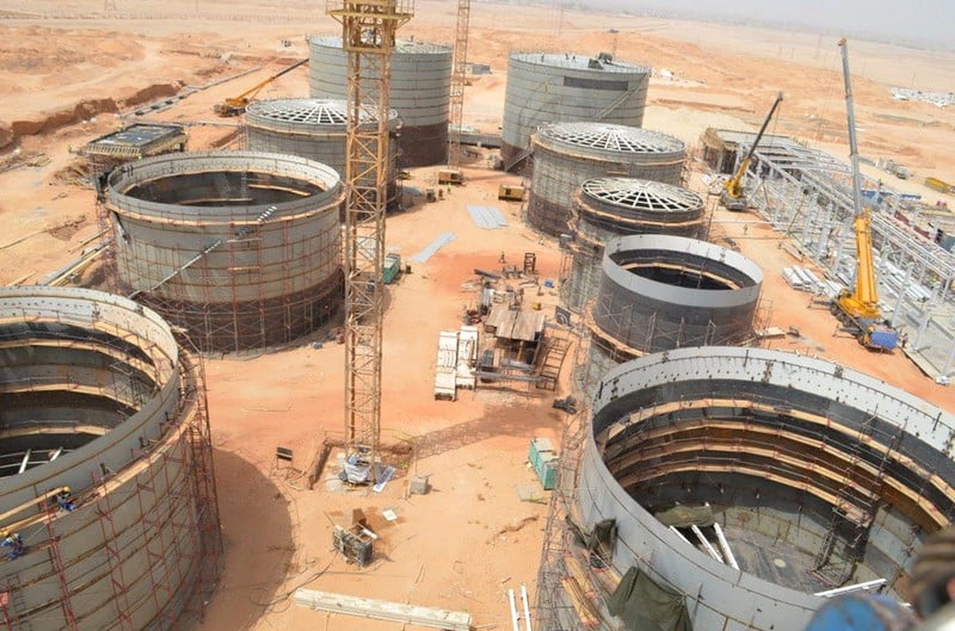 Aerial view of a tank farm under construction, with shell courses, open roof structures and a tower crane