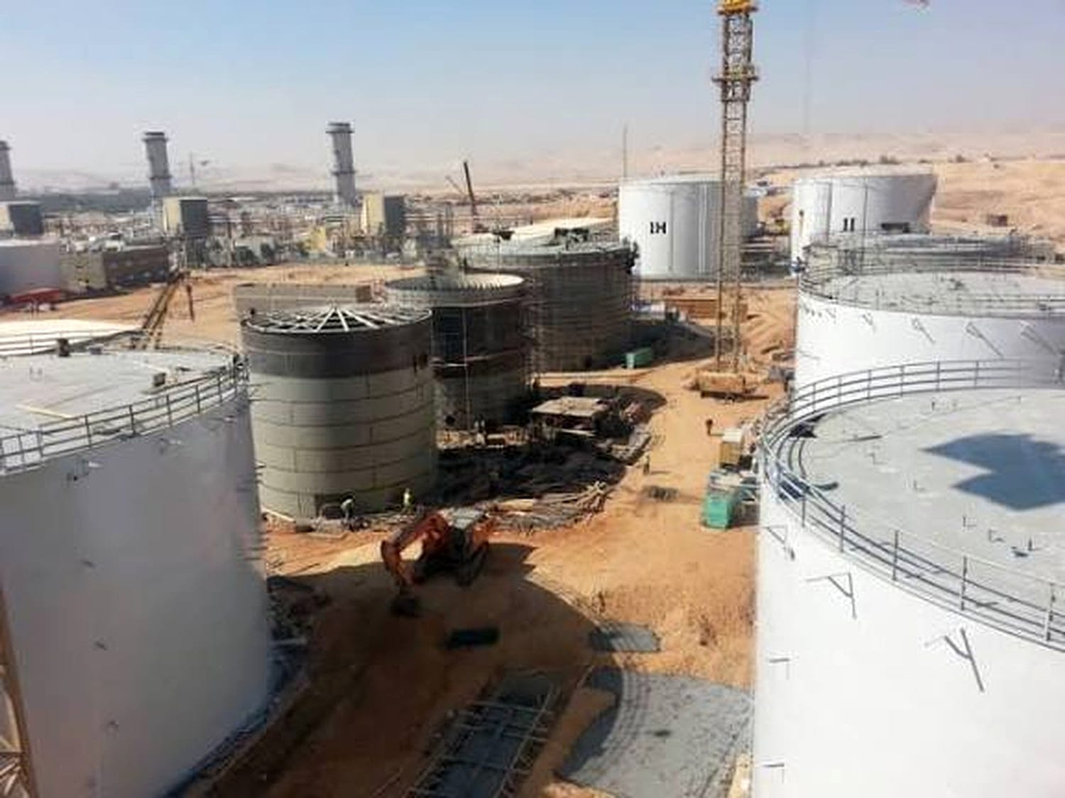 Ground-level view across a tank farm mid-erection, several tanks at different stages