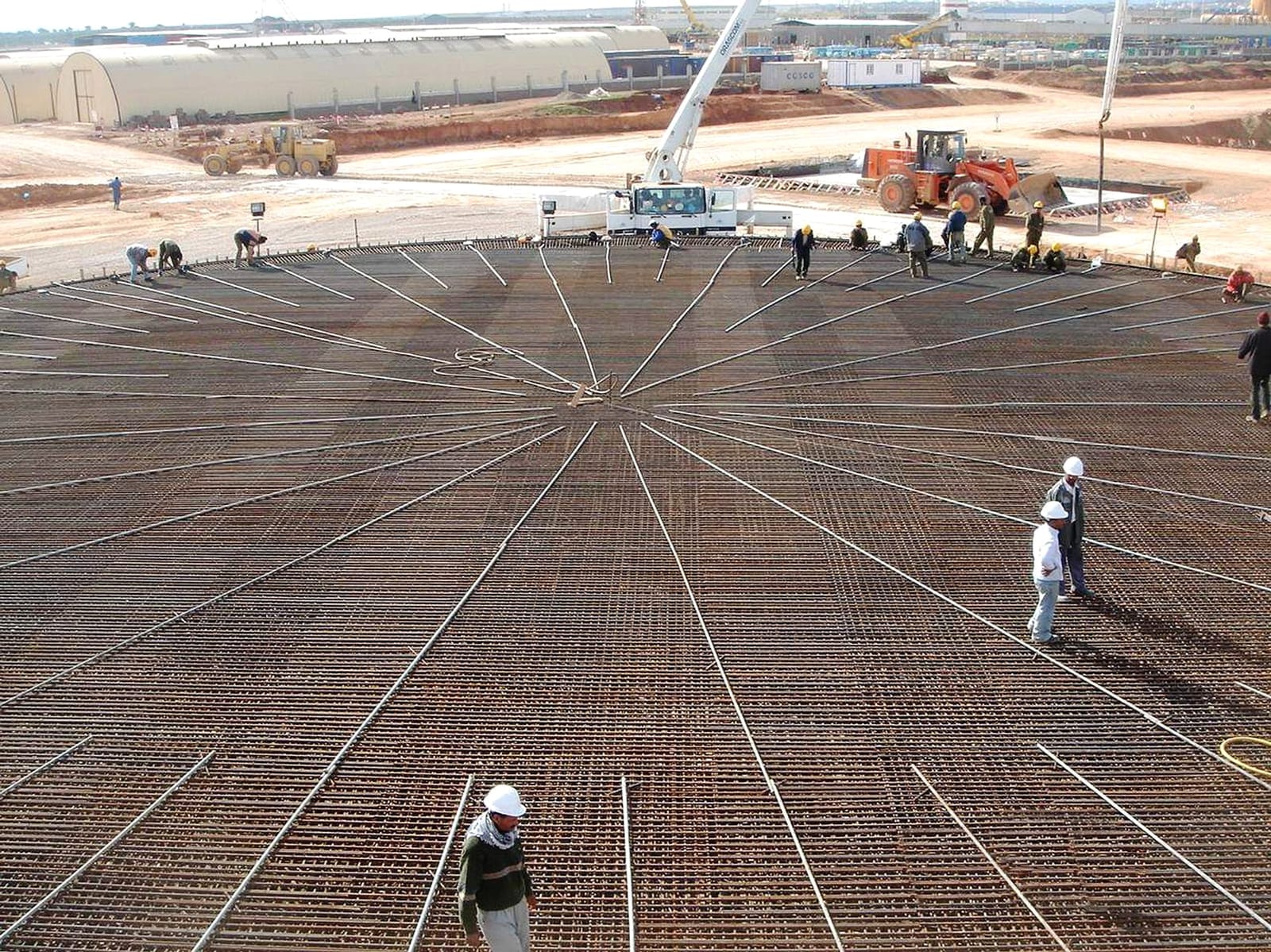 Radial reinforcement mat for a storage tank foundation, with workers and a mobile crane